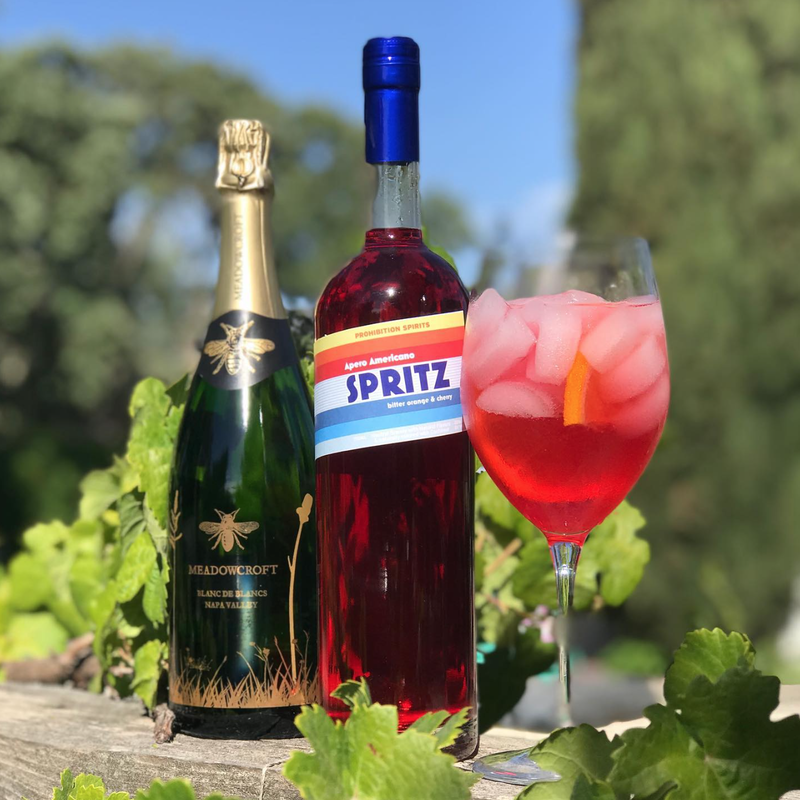 Spritz cocktail with liqueur and sparkling wine bottles on vineyard fence